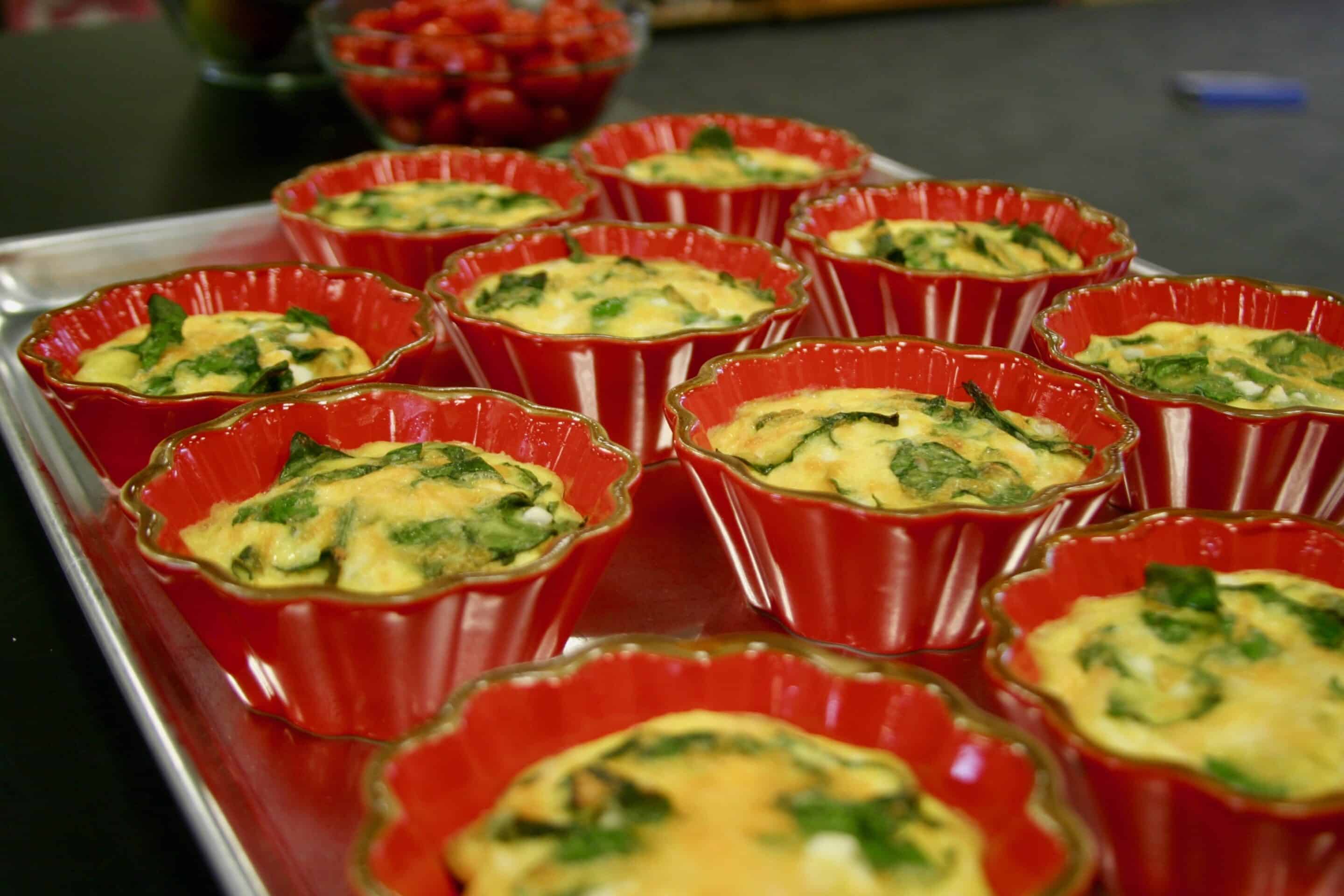A tray of red bowls filled with quiche.