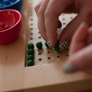 Close up of child's fingers working with small green beads on a peg board.