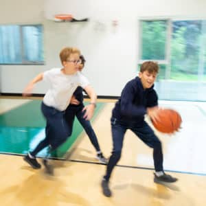 A group of Elementary children play basketball in the gym.