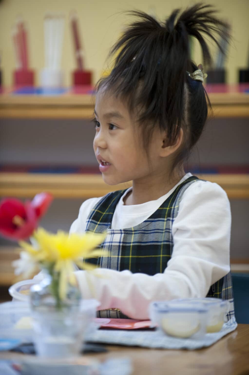 One Casa child setting her lunch containers out on a placemat in front of her, with her hair piled up on her head.