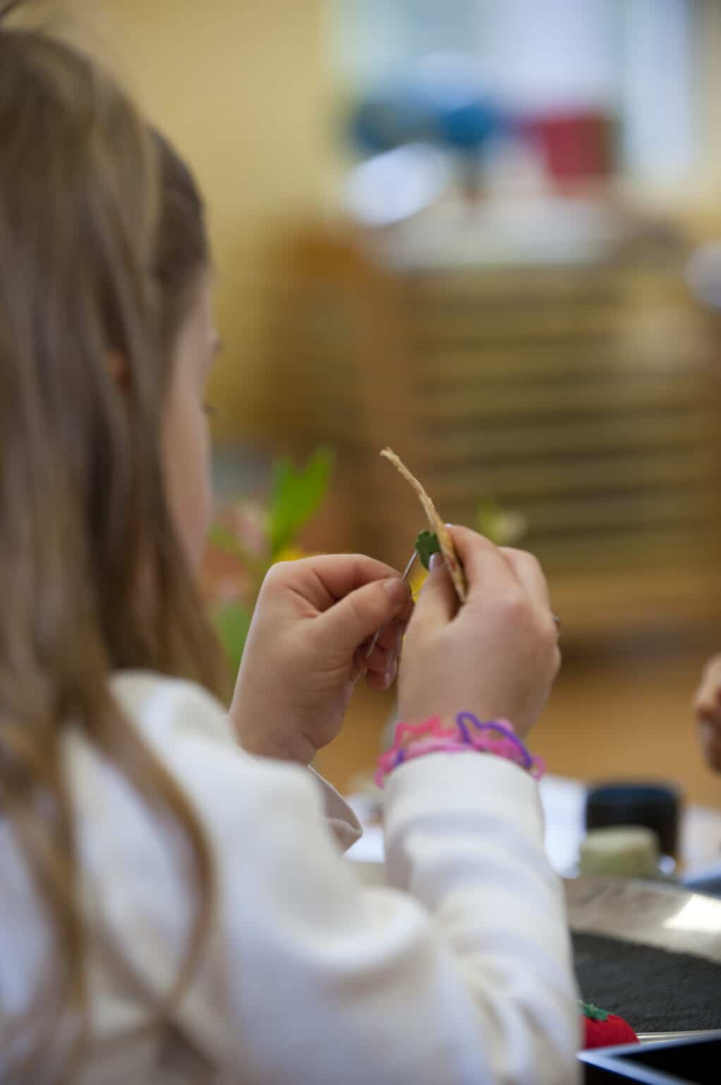 A view of a Casa child's hands, as she sews a button to a small square of fabric.