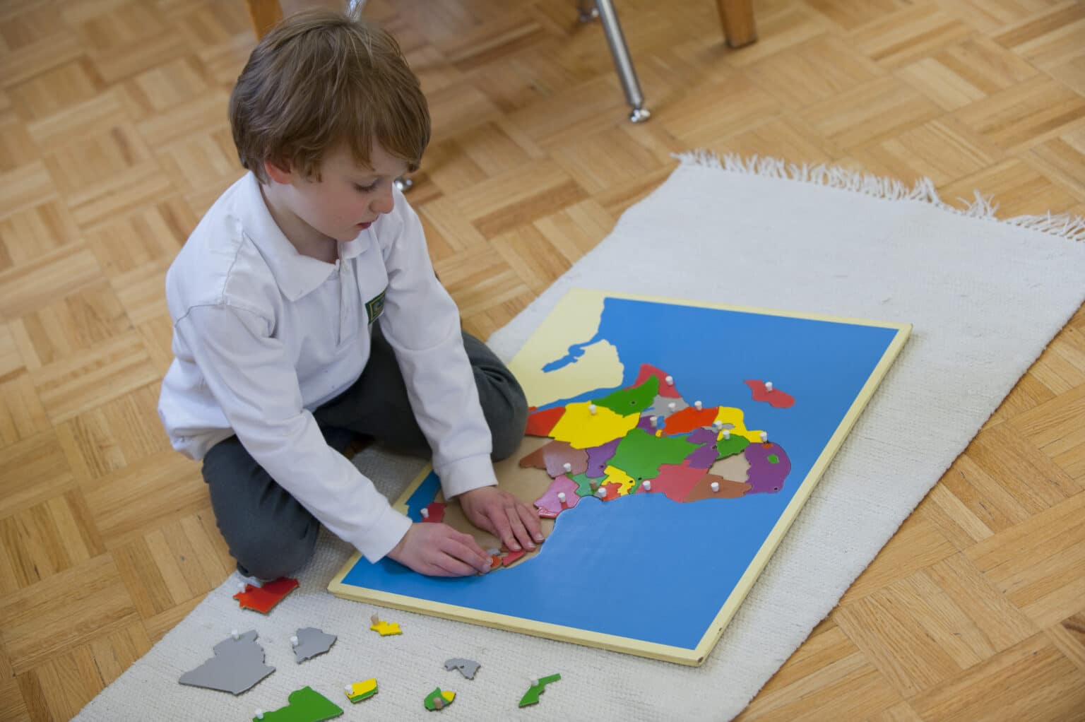 One Casa child work on a floor mat, arranging the pieces of a puzzle map of Africa.