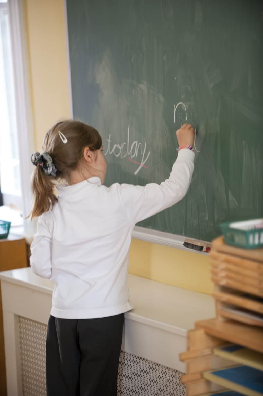 Elementary age child writing the date on a chalkboard in cursive script.