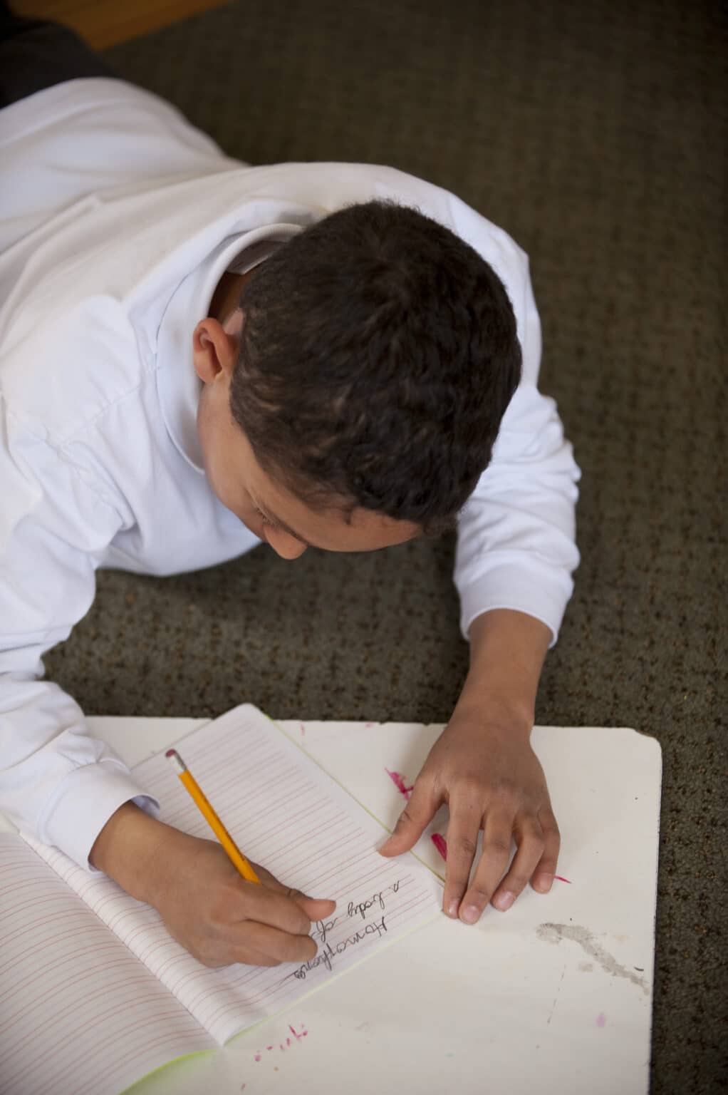 Elementary age child writing in cursive script in a lined notebook.