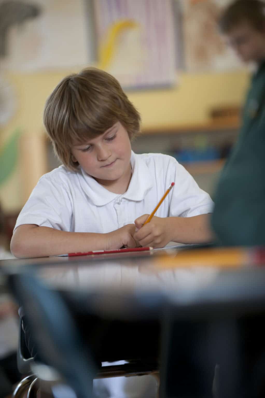 An Elementary child writes in his book with pencil, with great concentration on his face.