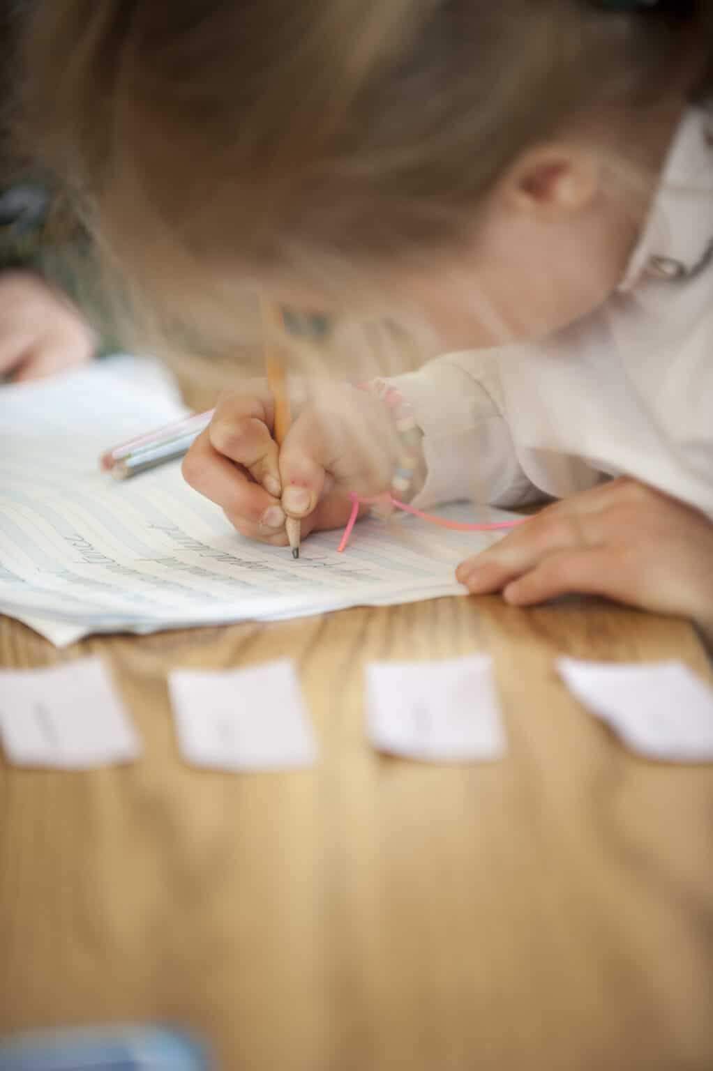 A closeup shot of an Elementary child copying words into her book, using cursive script.