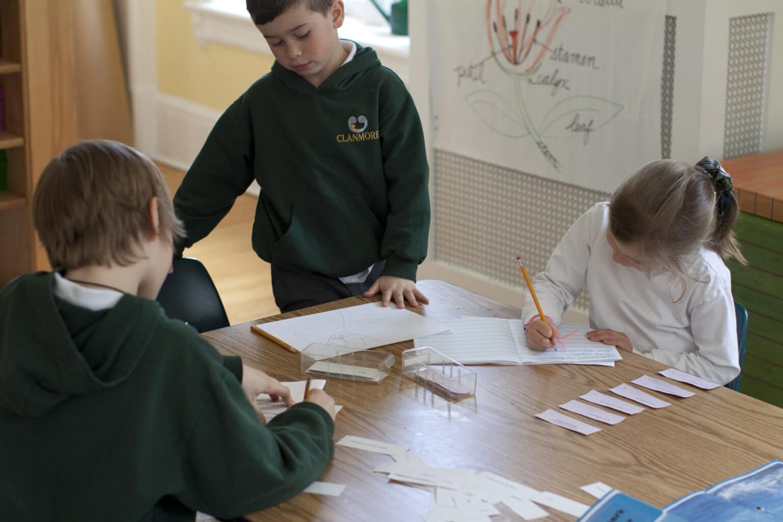 Three Elementary children work independently at the same table.