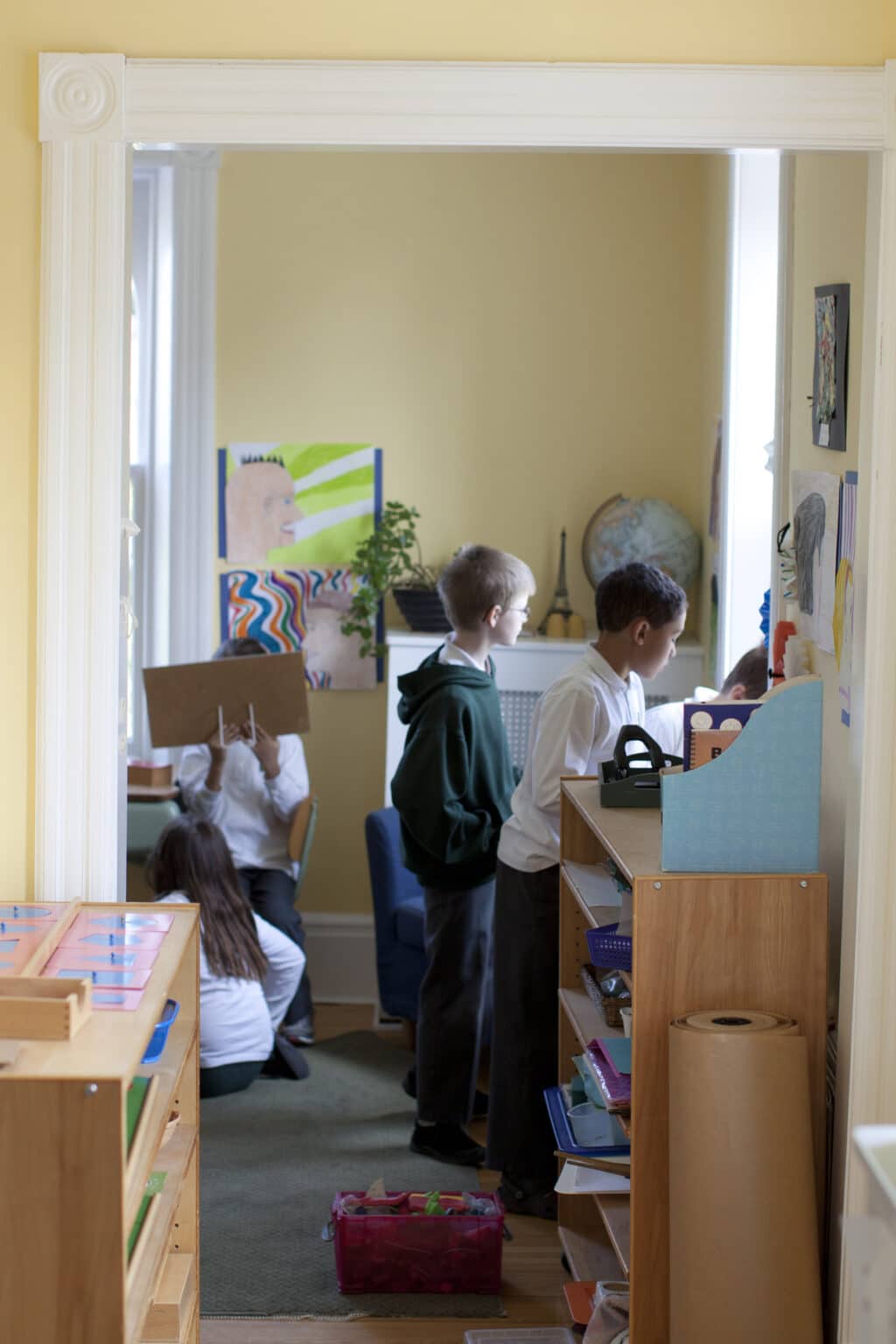 Three Elementary children look out the window, while others continue to work.