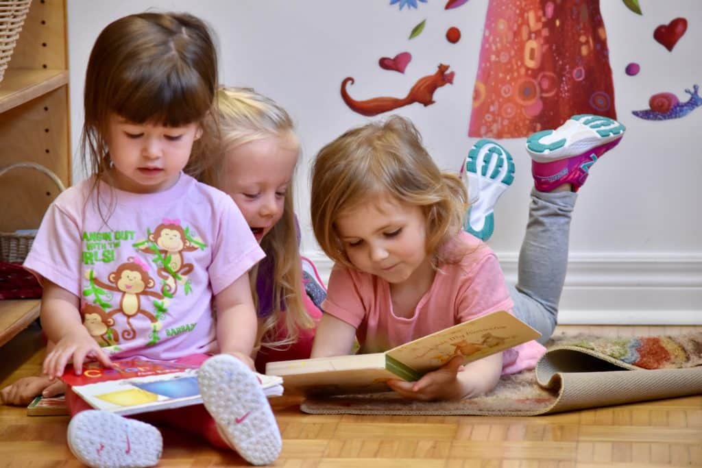 Three toddler students looking at books together.